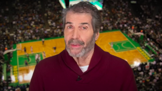 John Stossel is seen in front of a basketball court | Stossel TV